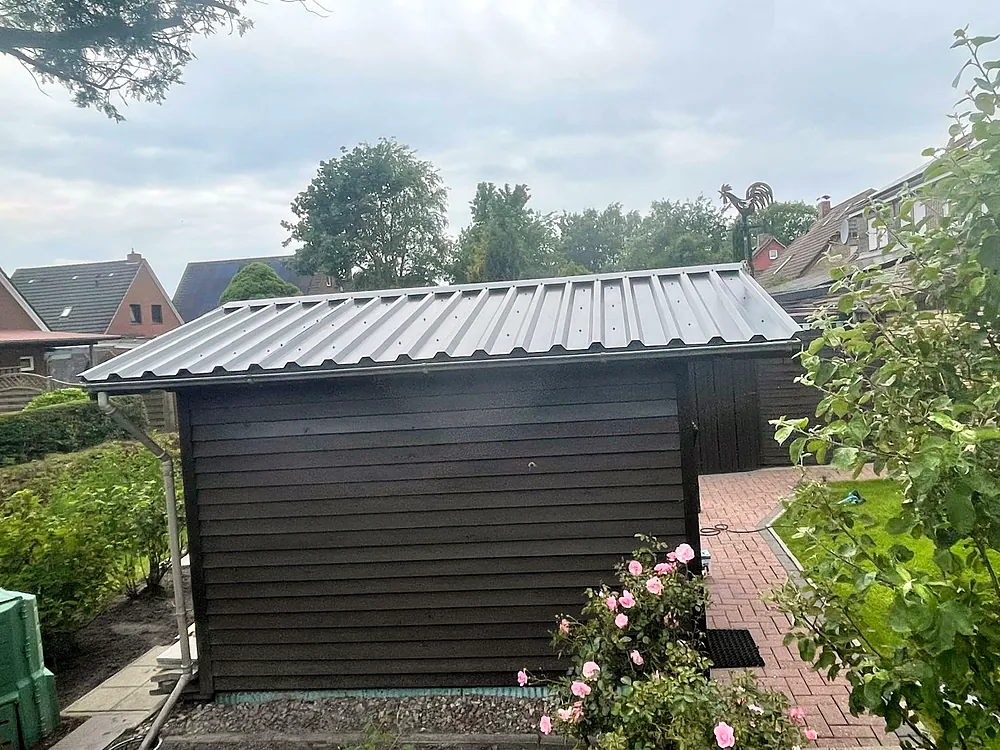 Gartenhaus mit Blechdach zwischen Rosen.